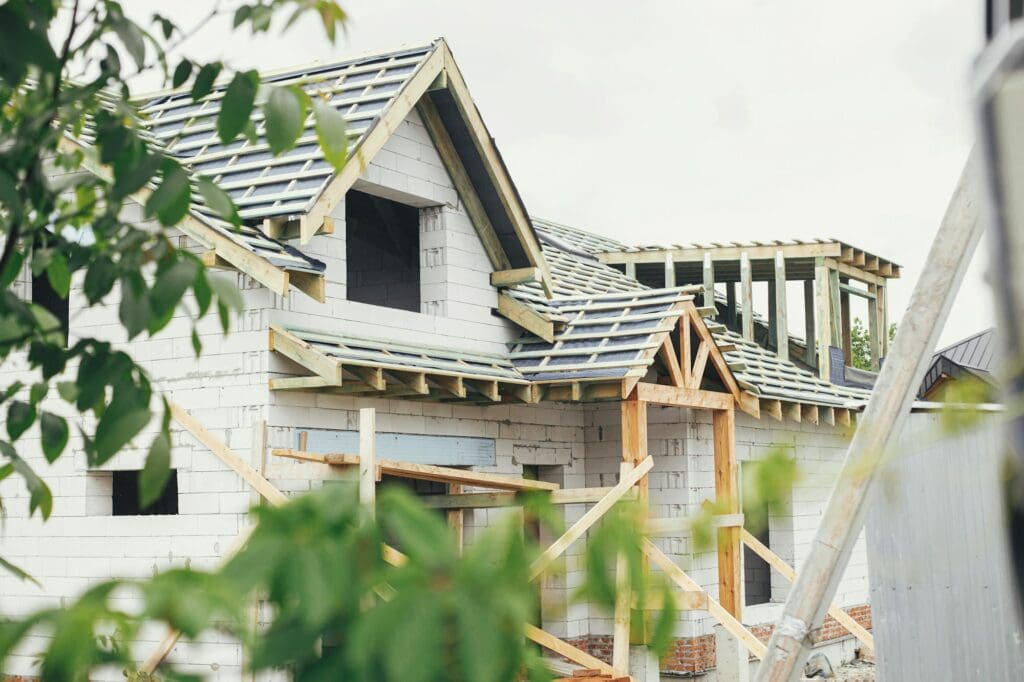 Unfinished modern farmhouse building. Wooden roof framing with dormer and vapor barrier